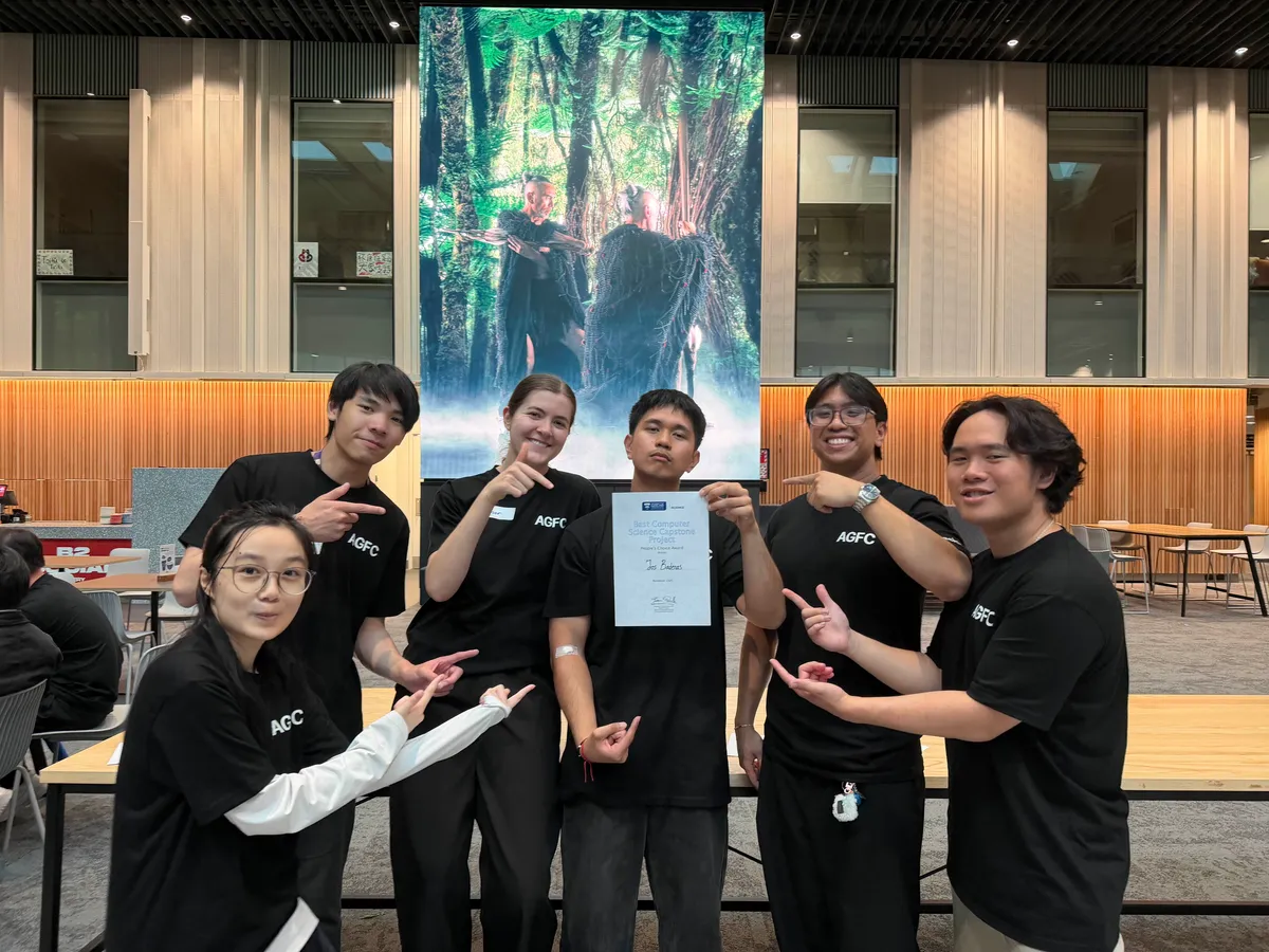 Six friends in black AGFC shirts pointing at Jos, who holds the People's Choice Award for Best Computer Science Capstone Project