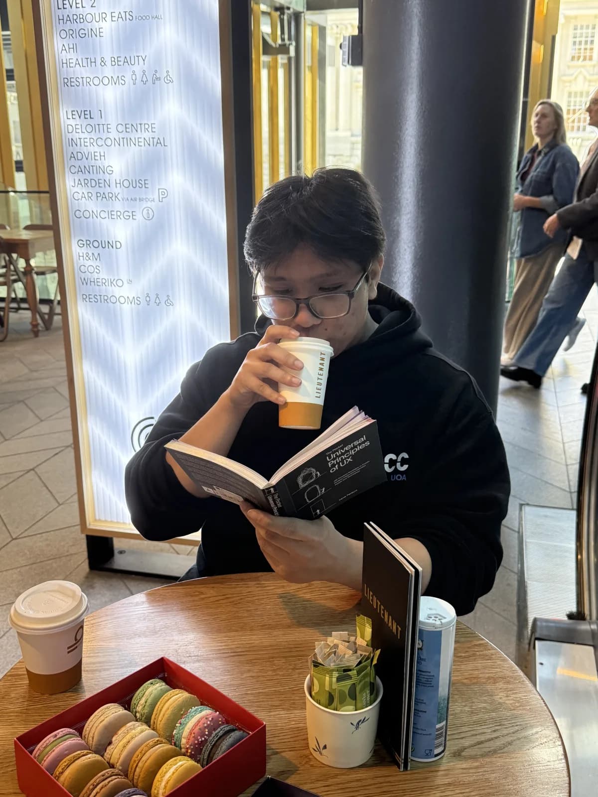 Anton at a café table, drinking a coffee and reading The Pocket Universal Principles of UX
